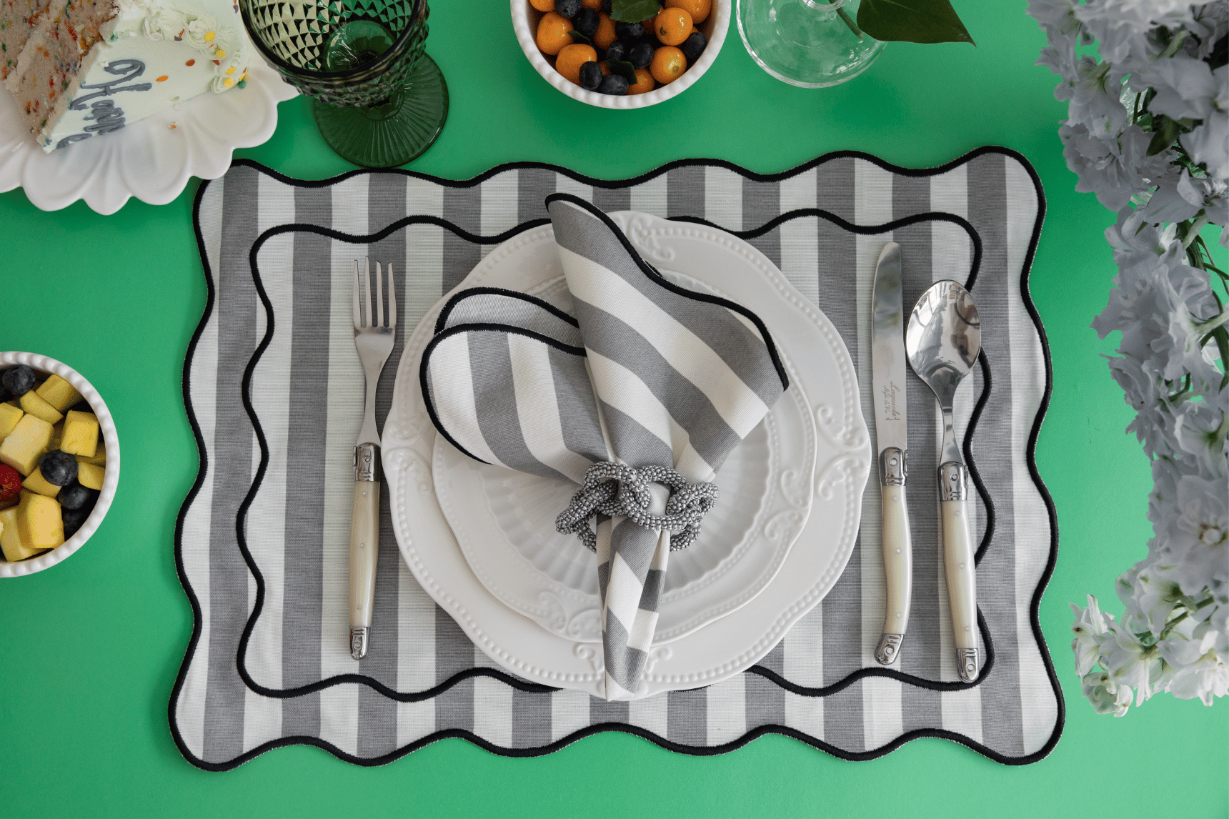 Table setting with gray and white striped placemat, white plates, silver cutlery, and a green background.